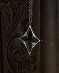 A sterling silver pendant with a stylized open quatrefoil, hanging from a chain against a dark brown carved wooden background.
