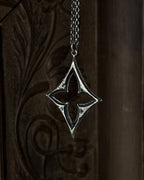 A sterling silver pendant with a stylized open quatrefoil, hanging from a chain against a dark brown carved wooden background.