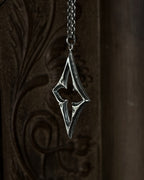 A sterling silver pendant with a stylized open quatrefoil, hanging from a chain against a dark brown carved wooden background.