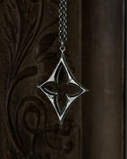 A sterling silver pendant with a stylized open quatrefoil, hanging from a chain against a dark brown carved wooden background.