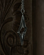 A sterling silver pendant with a stylized open quatrefoil, hanging from a chain against a dark brown carved wooden background.