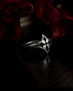 A silver-toned gothic ring with a stylized cross, resting on dark red dried flowers.