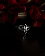 A silver-toned gothic ring with a stylized cross, resting on dark red dried flowers.