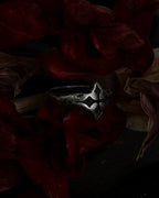 A silver-toned gothic ring with a stylized cross, resting on dark red dried flowers.