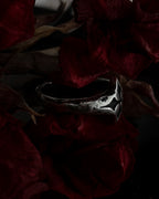 A silver-toned gothic ring with a stylized cross, resting on dark red dried flowers.