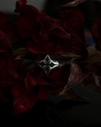 A silver-toned gothic ring with a stylized cross, resting on dark red dried flowers.