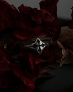 A silver-toned gothic ring with a stylized cross, resting on dark red dried flowers.