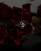 A silver-toned gothic ring with a stylized cross, resting on dark red dried flowers.